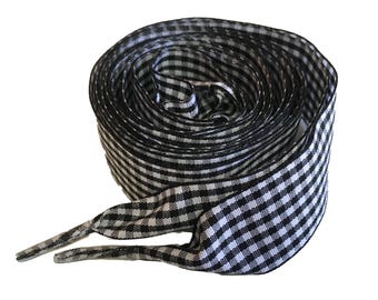 May include: Rolled-up black and white gingham shoelaces. The shoelaces are made of a woven fabric and have a classic checkered pattern. The ends are finished with aglets.