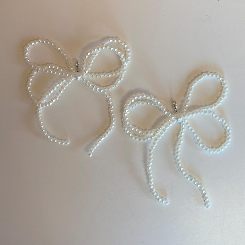 Puede incluir: Dos pinzas para el pelo con forma de lazo de perlas blancas. Cada pinza est&aacute; hecha de una cadena de perlas blancas atadas en forma de lazo.