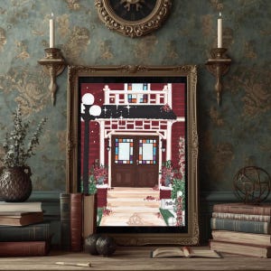 Puede incluir: Una impresi&oacute;n enmarcada de un edificio rojo con un porche blanco y un tejado negro. El edificio tiene puertas marrones con vidrieras. Una farola negra est&aacute; a la izquierda. La impresi&oacute;n est&aacute; en un marco dorado, sobre una superficie de madera con libros.