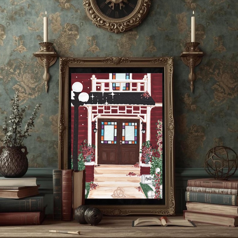 Puede incluir: Una impresi&oacute;n enmarcada de un edificio rojo con un porche blanco y un tejado negro. El edificio tiene puertas marrones con vidrieras. Una farola negra est&aacute; a la izquierda. La impresi&oacute;n est&aacute; en un marco dorado, sobre una superficie de madera con libros.