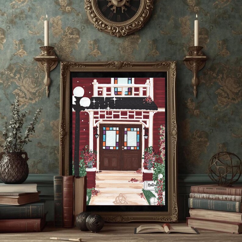 May include: A framed artwork depicts a red building with a white porch and stained glass windows. The artwork is in a gold frame and is displayed on a wooden surface with books, candles, and a decorative clock in the background.