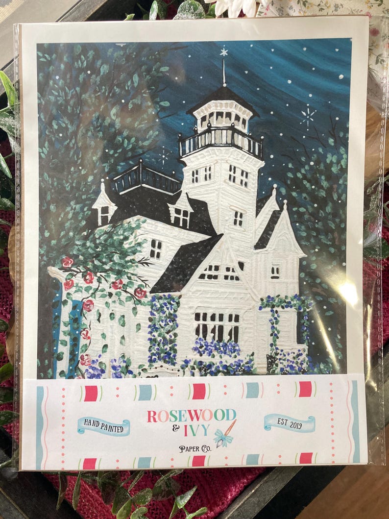 May include: Hand-painted art print of a white Victorian house with a tower, surrounded by lush greenery and flowers. The night sky is a deep blue with stars. The print is labeled "Rosewood & Ivy Paper Co."
