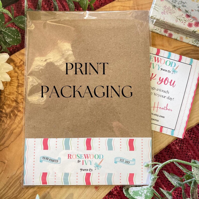 May include: Print packaging in a clear plastic sleeve. The brown paper packaging has the words "PRINT PACKAGING" in large black letters. A decorative label at the bottom reads "ROSEWOOD & IVY PAPER CO." with a floral design and the text "EST 2013".