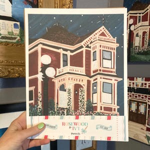 Puede incluir: Una impresi&oacute;n pintada a mano de una casa victoriana bajo un cielo estrellado. La casa est&aacute; pintada en tonos de rojo y crema, con una fachada y ventanas detalladas. La impresi&oacute;n incluye el texto "Rosewood & Ivy Paper Co. EST 2013".