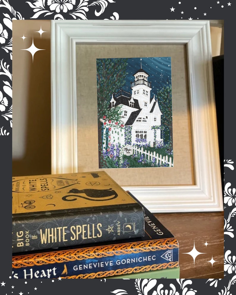 May include: A framed painting of a white house with a tower, surrounded by a white picket fence and flowers. The painting is in a white frame, and is set on a table with a stack of books, including one titled "Big Book of White Spells".