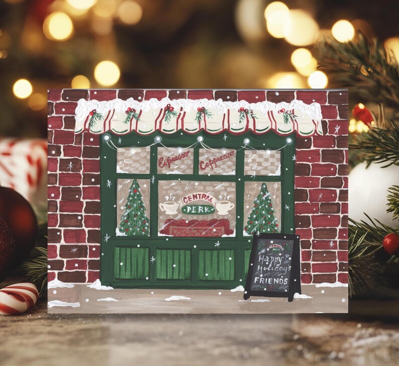 K&ouml;nnte beinhalten: Weihnachtliche Illustration des Caf&eacute;s Central Perk mit roter Backsteinfassade, gr&uuml;nen Verzierungen und einem kleinen Tafelschild mit der Aufschrift "Happy Holidays Friends". Das Caf&eacute; hat eine festliche Markise und Weihnachtsb&auml;ume.