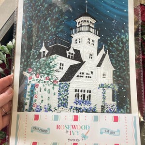 May include: A hand-painted art print of a white Victorian house with a tower, surrounded by lush greenery and blue flowers. The night sky is a deep blue with stars. The print is labeled "Rosewood & Ivy Paper Co."