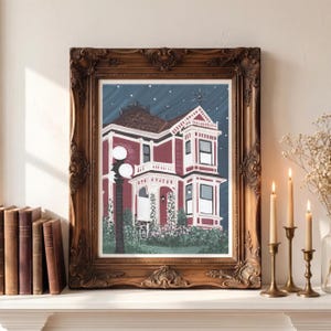 Puede incluir: Una pintura enmarcada de una casa victoriana con exterior rojo y adornos blancos, sobre un cielo estrellado. El marco ornamentado, de color marr&oacute;n oscuro, complementa la obra de arte. La pintura se exhibe en una repisa blanca, con velas y libros cerca.