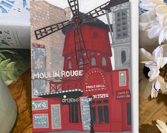 May include: A red and white Moulin Rouge art print. The image features the iconic Parisian cabaret with its windmill and signage. The words "MOULIN ROUGE" and "MUSIC HALL" are visible. The artwork is on a white card.