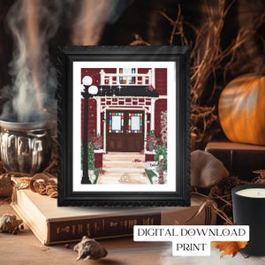 May include: A framed print of a red house with a black frame. The house has a dark brown door and colorful stained glass windows. The print is labeled "DIGITAL DOWNLOAD PRINT". The print is on a stack of books with a candle and a pumpkin in the background.