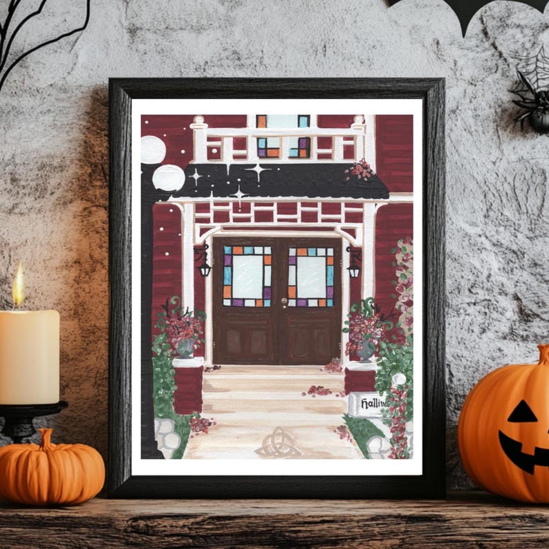 Puede incluir: Una impresi&oacute;n enmarcada de una casa burdeos con un porche blanco y vidrieras. La obra de arte presenta un tema de Halloween, con calabazas, una vela y una telara&ntilde;a. La impresi&oacute;n se exhibe en un estante de madera.