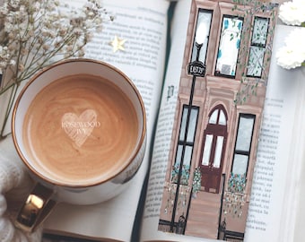 May include: A rectangular bookmark featuring a detailed illustration of a brownstone building facade with a dark arched door, windows with flower boxes, and a street lamp sign reading East 75. The artwork uses shades of brown, cream, and green.