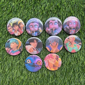 May include: A collection of ten round pinback buttons with colorful illustrations. The buttons feature various anime-style characters, including portraits and action scenes. The buttons are arranged on a bed of green grass.