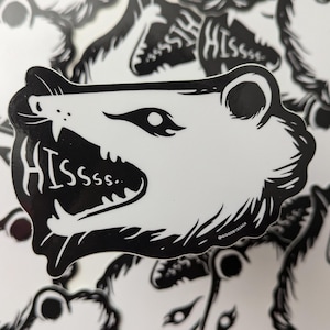 May include: Black and white sticker of an animal's face with sharp teeth and the word "HISSsss." printed below.