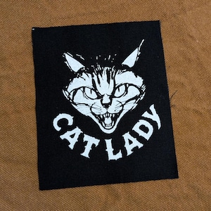 May include: Black and white iron-on patch with a cat face and the text "CAT LADY".