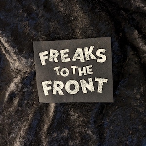 May include: Black fabric patch with white text that reads "FREAKS TO THE FRONT".