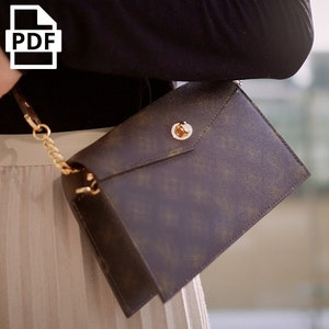 May include: A brown leather envelope-style crossbody bag with a gold chain strap and a gold clasp.