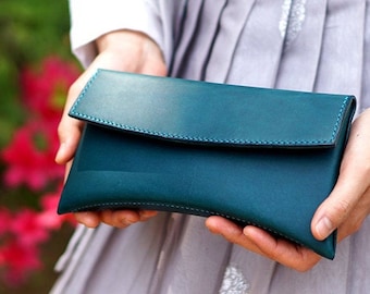 May include: A teal blue leather clutch purse with a flap closure and a subtle stitch detail.