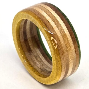 May include: A handcrafted wooden ring with a unique design. The ring features alternating layers of light and dark wood, with a green accent. The ring has a smooth, polished finish and a width of approximately 0.3 inches.
