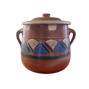 May include: A terracotta pot with a lid, featuring a geometric design in blue, white, and black. The pot has two handles and is decorated with a repeating pattern of triangles and arches.