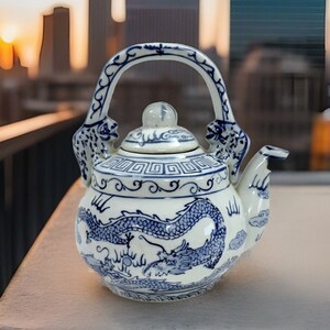 May include: A white porcelain teapot with a blue and white dragon design. The teapot has a lid and a handle with a dragon design. The teapot is decorated with clouds and a border of geometric patterns.