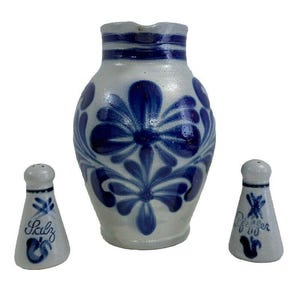 May include: A set of three blue and white ceramic salt and pepper shakers with floral designs. The larger shaker is a pitcher with the word "Salz" on it. The smaller shakers are labeled "Pfeffer".