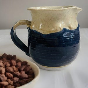 May include: A handmade ceramic pitcher with a blue and white glaze. The pitcher has a wide mouth and a handle. It is perfect for serving milk, cream, or juice.