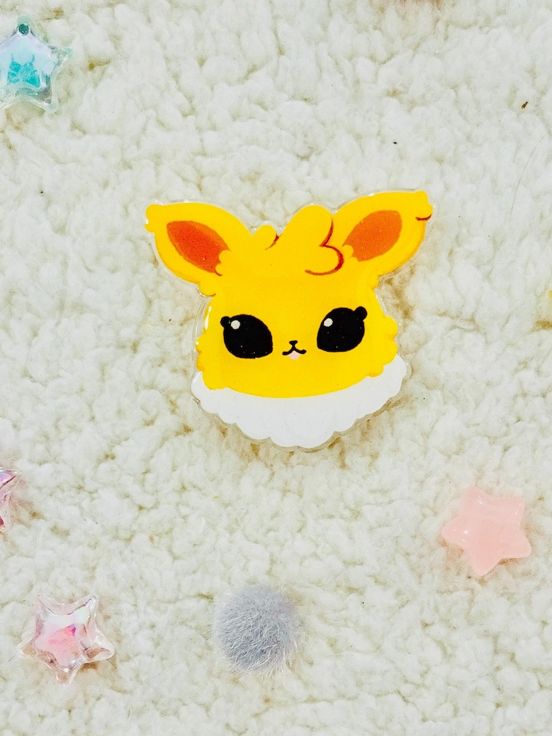 Puede incluir: Un personaje de dibujos animados amarillo y naranja con ojos grandes y un cuello blanco esponjoso. El personaje es un pin hecho de acr&iacute;lico transparente.