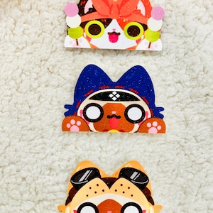 May include: Three colorful cartoon cat faces with different accessories. The top cat is wearing a red bow and holding a dango on a stick. The middle cat is wearing a blue ninja headband. The bottom cat is wearing sunglasses.
