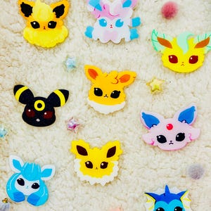 May include: Nine colorful cartoon Pokemon character pins. The pins are made of clear acrylic and feature different Pokemon characters, including Eevee, Vaporeon, Jolteon, Flareon, Espeon, Umbreon, Leafeon, Glaceon, and Sylveon.
