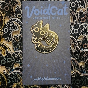 May include: A gold-colored enamel pin in the shape of a cat, with a starry design and the text "VoidCat enamel pin." The pin is on a dark gray card with the text "inthebluemoon."