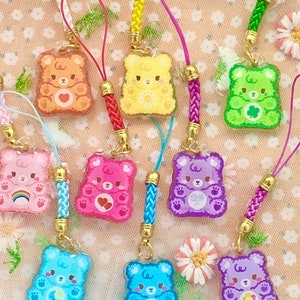 May include: Nine colorful bear-shaped charms with different designs, each attached to a braided string with a gold clasp. The charms are translucent and feature various colors, including orange, yellow, green, pink, purple, and blue.