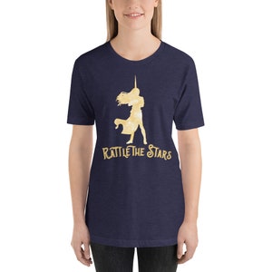 Puede incluir: Una camiseta azul marino con una silueta dorada de una mujer sosteniendo una espada y el texto "Rattle the Stars".