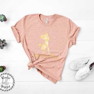 Puede incluir: Una camiseta de color melocot&oacute;n con una silueta dorada de una mujer sosteniendo una espada y el texto "To the Stars".