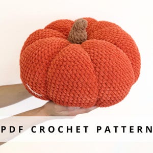 Op de afbeelding: Een gehaakte pompoen in oranje met een bruine steel. De pompoen is rond en heeft een getextureerd oppervlak. De tekst "PDF CROCHET PATTERN" wordt onderaan de afbeelding weergegeven.