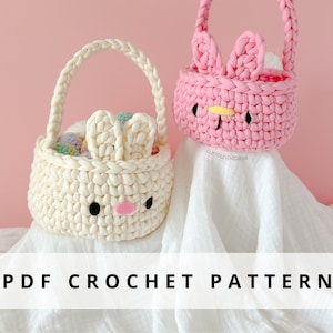 以下が含まれることがあります： 白い背景に、白とピンクの2つの編みぐるみウサギのバスケット。バスケットはカラフルなイースターエッグでいっぱいです。画像の下部に「PDF CROCHET PATTERN」というテキストがあります。