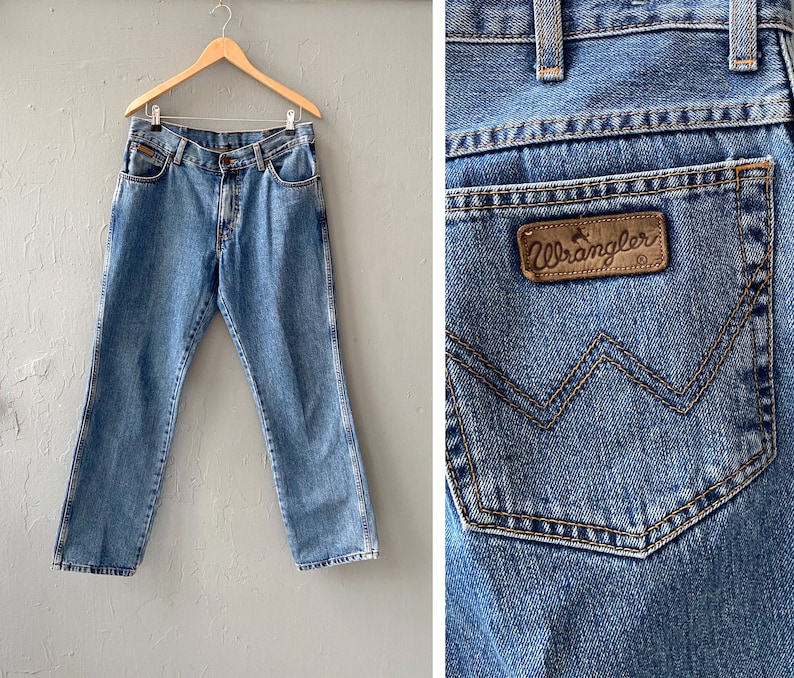 Pu&ograve; includere: Un paio di jeans blu in denim con un'etichetta Wrangler in pelle marrone sulla tasca posteriore. I jeans hanno una vestibilit&agrave; classica a gamba dritta e una chiusura con bottoni.