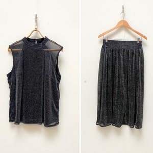 Könnte beinhalten: Ein zweiteiliges Outfit aus schwarzem und silbernem Glitzerstoff. Das Oberteil ist ein ärmelloses Tanktop mit einem durchsichtigen Überzug. Der Rock ist ein Midirock mit hoher Taille.