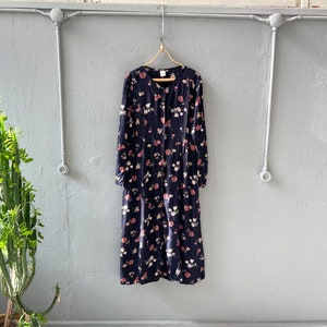 K&ouml;nnte beinhalten: Ein lang&auml;rmeliges, marineblaues Kleid mit einem Blumendruck mit rosa und wei&szlig;en Blumen. Das Kleid hat einen Knopfleisten vorne und eine lockere Passform.