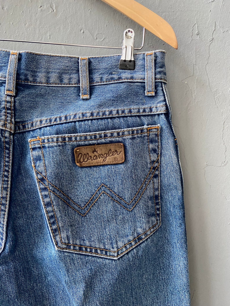 Pu&ograve; includere: Un paio di jeans blu denim con una toppa in pelle marrone Wrangler sulla tasca posteriore.
