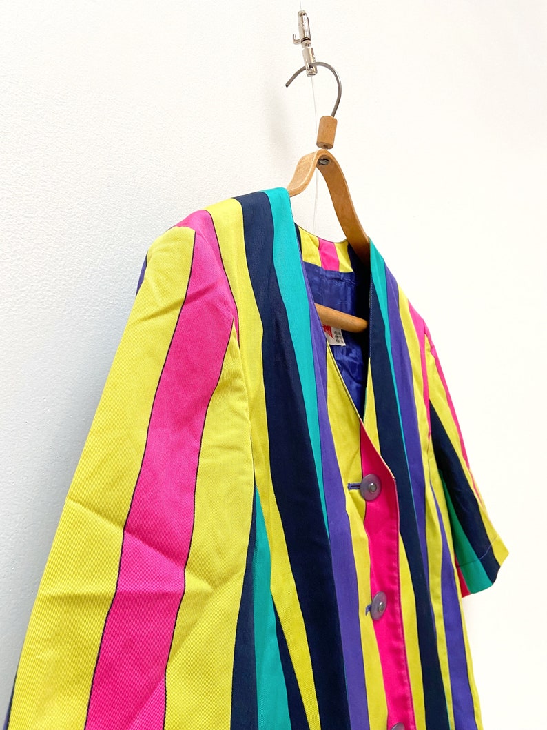 May include: A striped blazer with yellow, pink, blue, purple and green stripes. The blazer has a button closure and short sleeves.