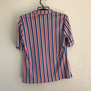 May include: A striped short-sleeved shirt with red, blue, and white vertical stripes. The shirt has a button-up collar and is hanging on a hanger.