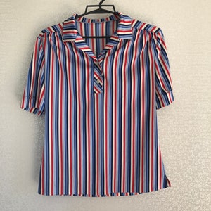 May include: A striped short-sleeved shirt with a collared neckline and a single button closure. The shirt is white with red, blue, and light blue stripes.