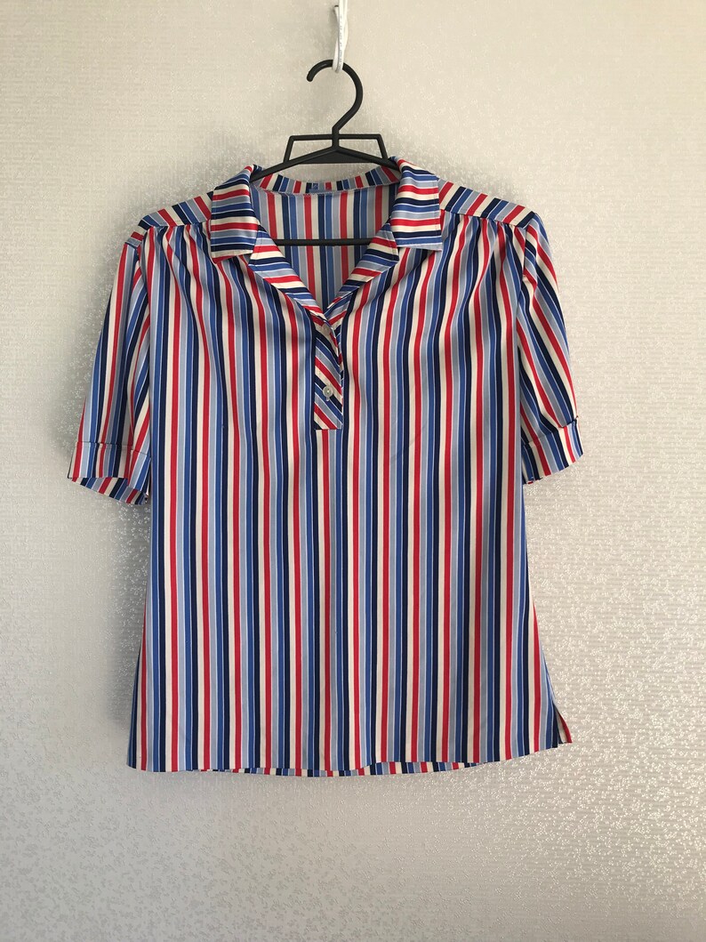 May include: A striped short-sleeved shirt with a collared neckline and a single button closure. The shirt is white with red, blue, and light blue stripes.