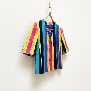 May include: A short-sleeved, multi-coloured striped blazer with a V-neck and button closure. The blazer is hanging on a wooden hanger against a white background.