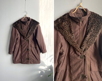 Könnte beinhalten: Eine braune Winterjacke mit Kunstfellbesatz, Reißverschluss und Druckknöpfen. Die Jacke hat einen großen Kragen und eine lockere Passform.