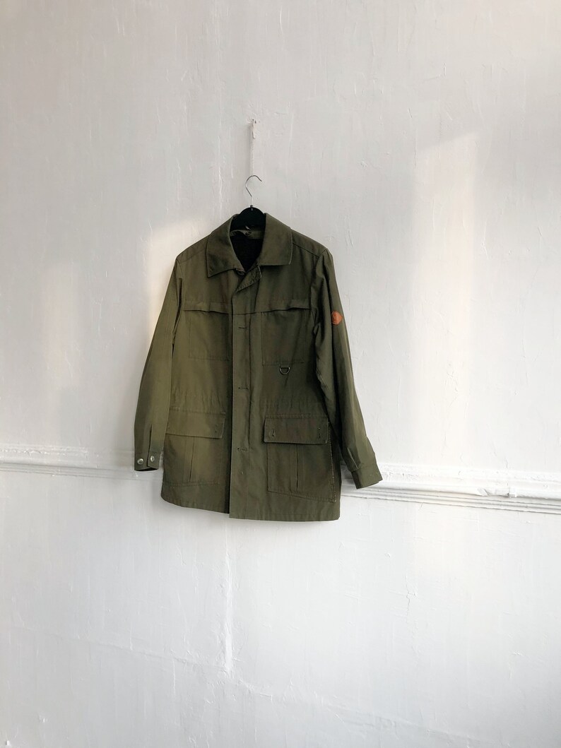 May include: A green utility jacket with a patch on the right sleeve and a button closure.