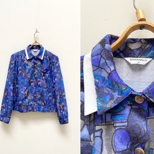 May include: A blue and white patterned button-up shirt with a white collar. The shirt has a geometric pattern and the label "Markwald 42" is visible.