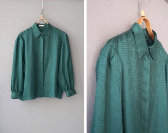 May include: Emerald green long-sleeve button-down shirt with a textured pattern. The shirt features a classic collar and cuffs, hanging on a wooden hanger against a gray background. The fabric has a subtle paisley and houndstooth design.
