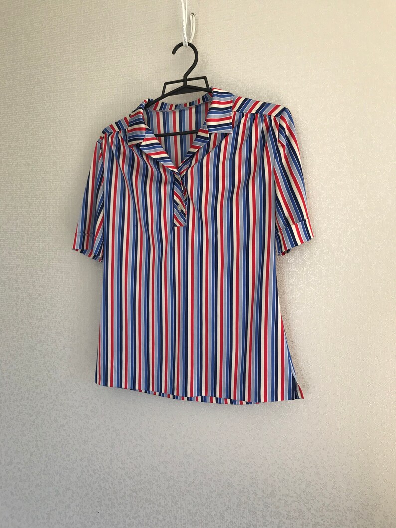May include: A striped short-sleeved shirt with a collar and button closure. The shirt is white with red, blue, and light blue stripes.